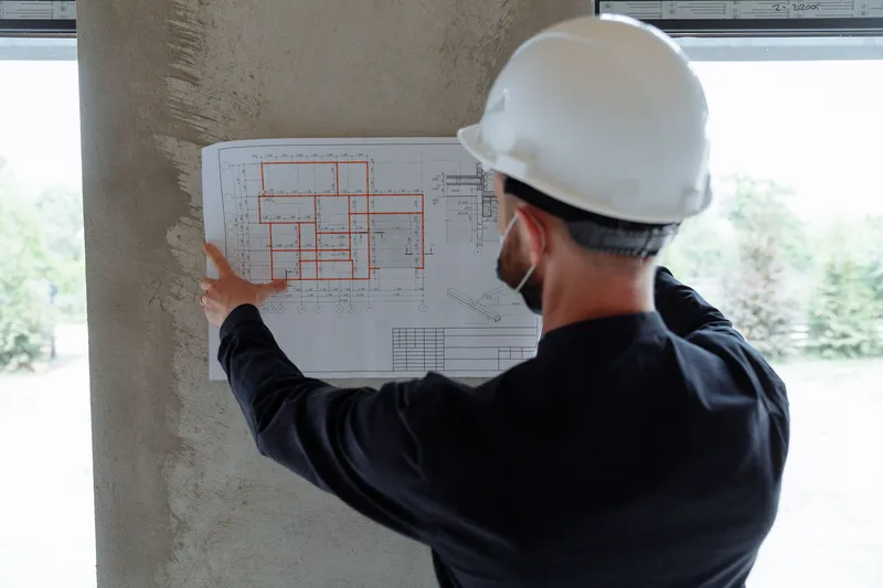 Arquitecto con casco revisando planos impresos contra la estructura de concreto en obra